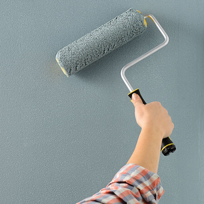 A hand holds a paint roller, completing the application of green paint on a wall.