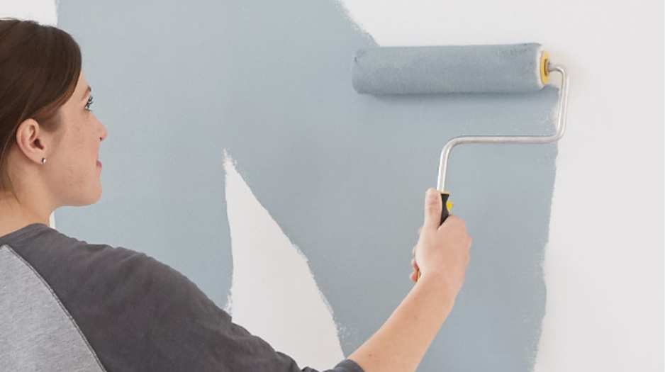  A woman happily applies light grey paint to a white wall using a paint roller.