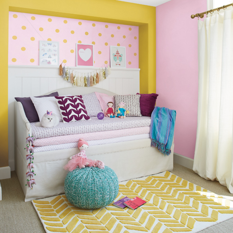 A whimsical nursery with a comfy trundle, a white cat and a playful yellow polka dot pattern on a pink wall.