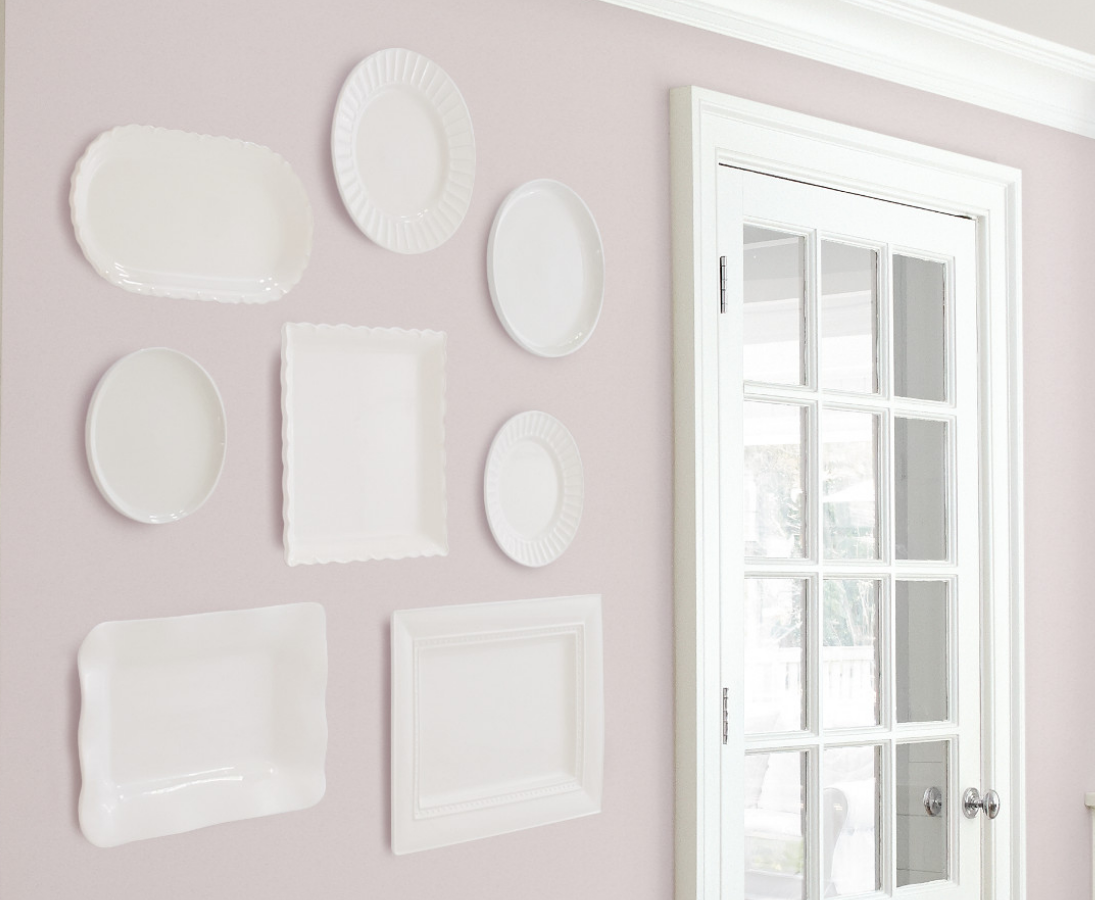 Decorative white dishes act as wall art in a living room with mauve walls and a glass framed door.