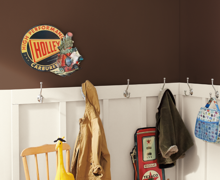 Mudroom with jackets and bookbag hanging on hooks, a vintage railroad sign on wall, white wainscoting.