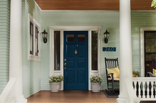 Front porch of a home with rocking chairs. A blue front door and teal siding give way to the porch, painted sweetened tea.