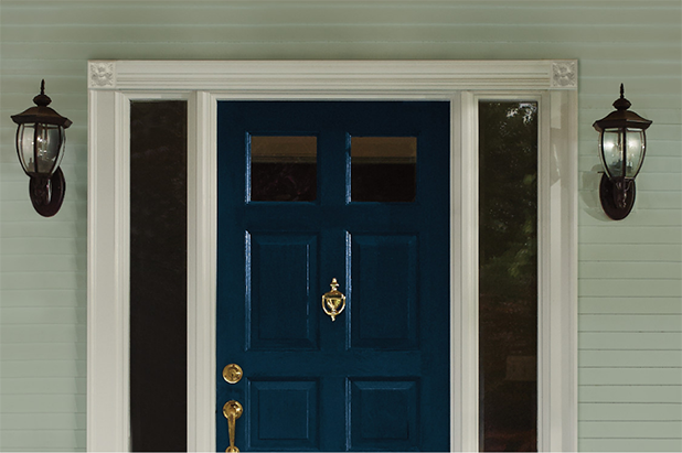 Tight shot of a front door painted blue with gold hardware, teal siding on the home.