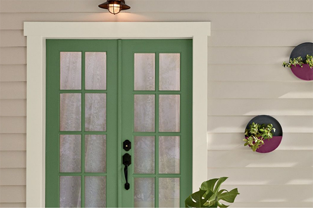 Back patio with green French doors, a sconce lit above it, with beige siding and white trim.