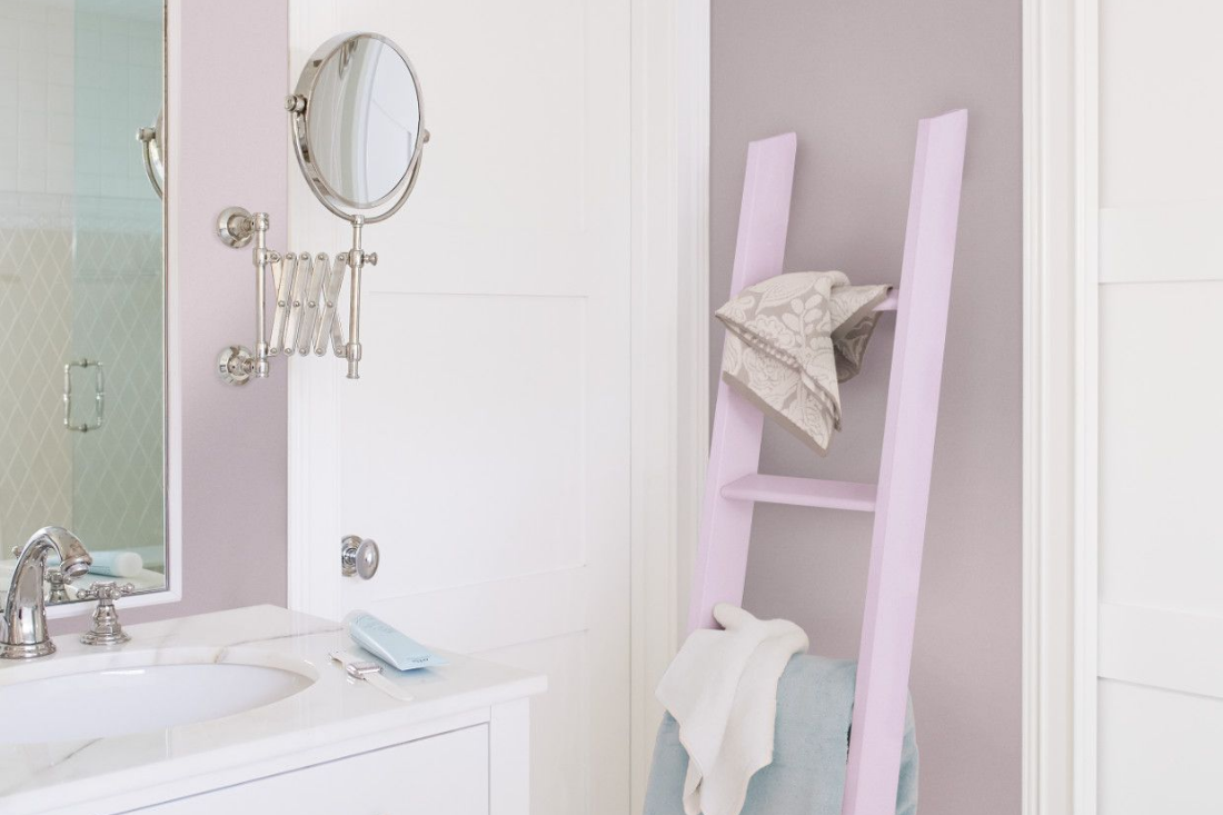 A light pink ladder shelf sits against the wall of a bathroom with traditional silver faucet and accessories on the vanity.