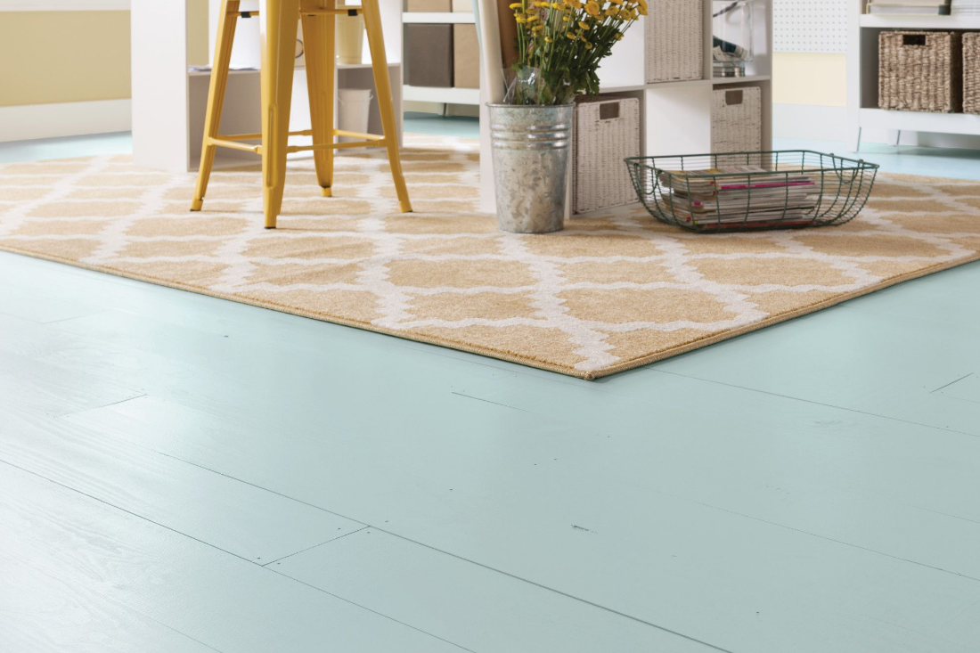 Wood flooring painted a light teal color, brightening the room, pairing nicely with a yellow chair and area rug.