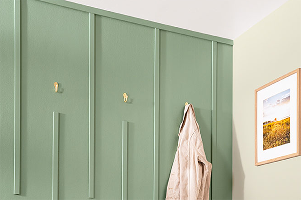 Entryway wall painted light green, with gold hooks holding a jacket and a framed color photograph on adjacent wall.