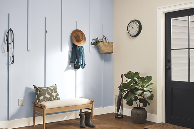 Entryway with hooks on whispered-colored walls, hanging a jacket and hat. Sitting bench with boots on ground in front of it.