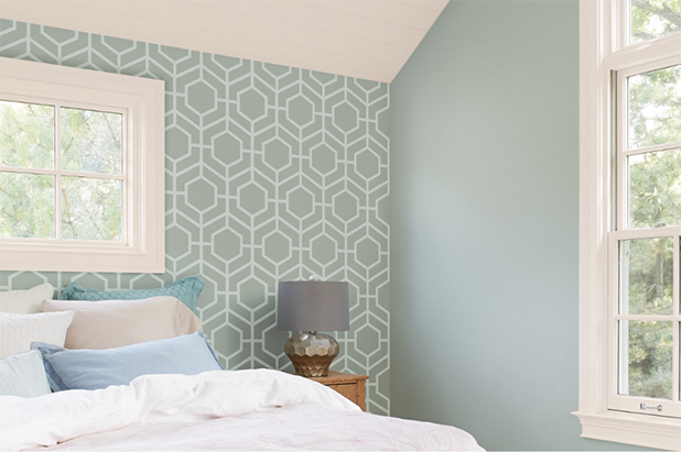 A bedroom with a stenciled geometric pattern in white on a light green wall.