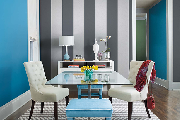 A dining room with furniture and accents has a striped accent wall painted the colors charcoal black and dusky grey. 