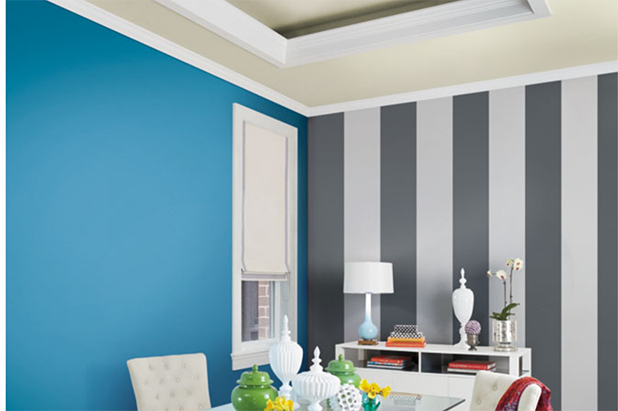 Dining room with a glass dining table, white buffet, stylish chairs, blue walls and a striped accent wall in grey and white. 