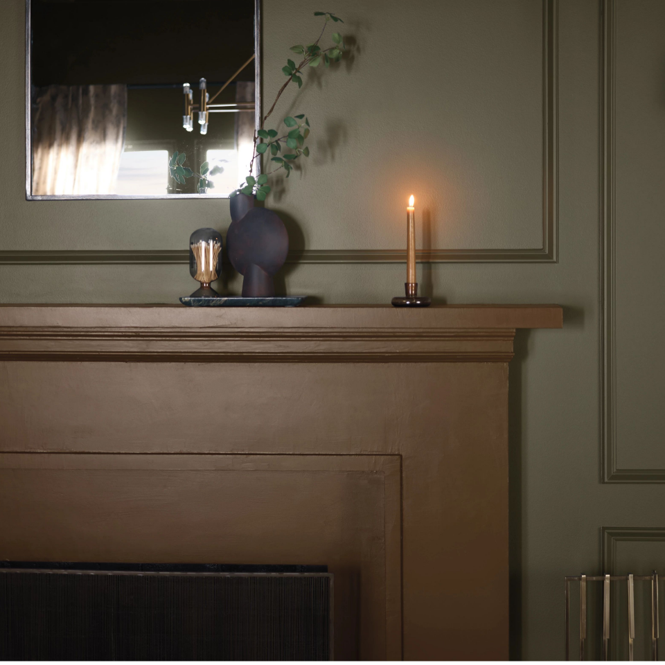 Candlelit, dark living room with a mirror reflecting light from windows. Mantel is painted heritage brown. 