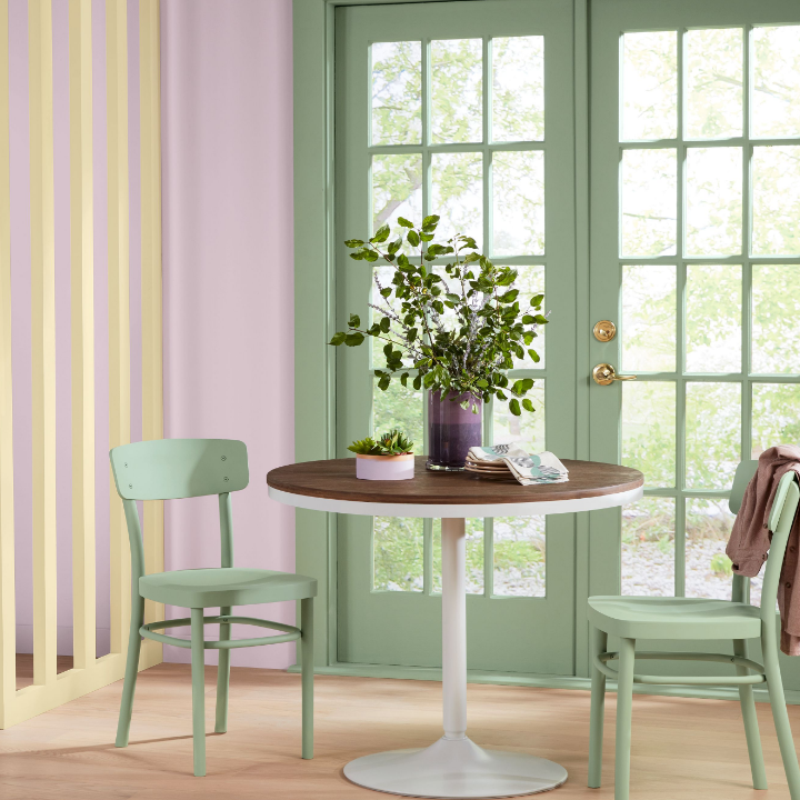 Small dining table sits in front of French doors painted in a pale green. The rest of the walls are painted shadowed rose.