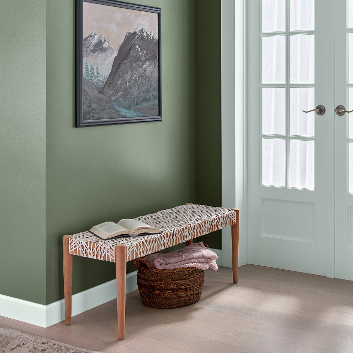 Entryway with modern bench seat and basket that holds blankets. Framed art hangs on the wild basil colored wall.