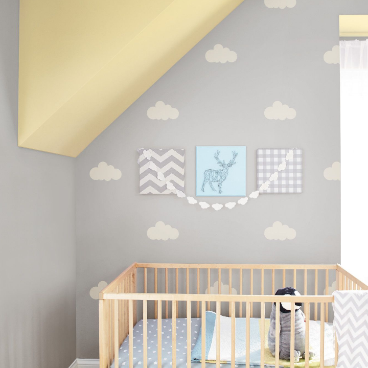 A nursery decorated with a natural wood crib and simple canvas prints on the fair-minded gray wall.