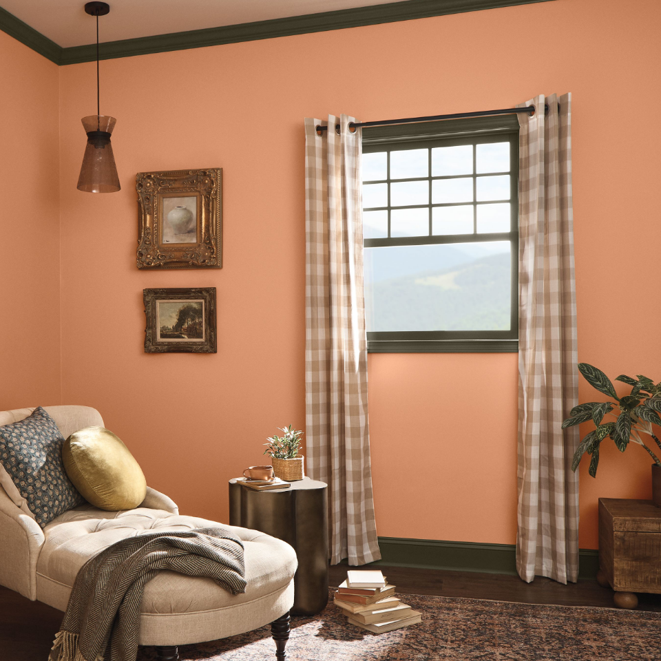 Sitting room with a chair with the sun shining through a wood framed window. Walls painted the color wild orange.