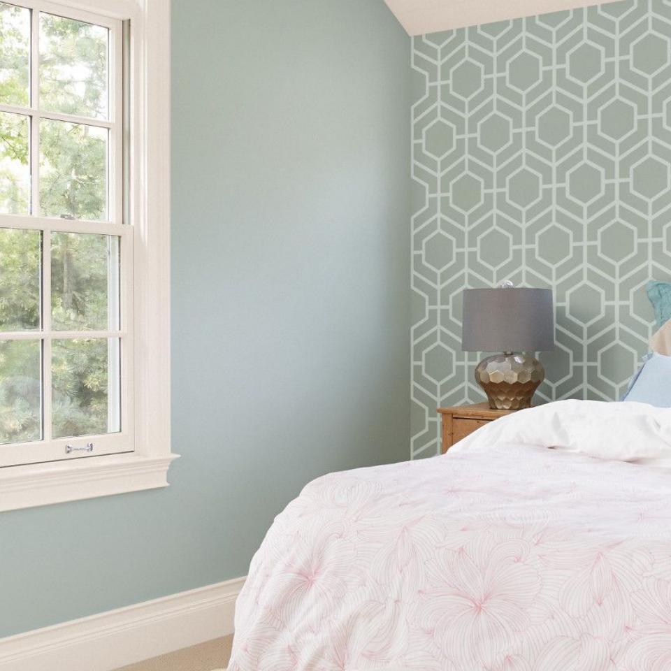 Sunny bedroom with lighter tones and patterned wallpaper on one wall. Adjacent wall is painted coastal mist.