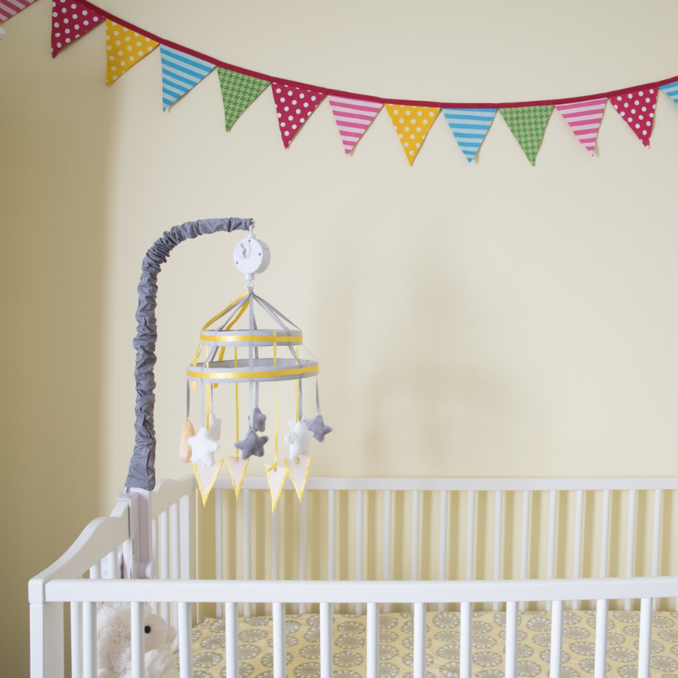 Nursery painted yellow with white crib and a mobile above it. A multi-colored pennant is draped across the wall.