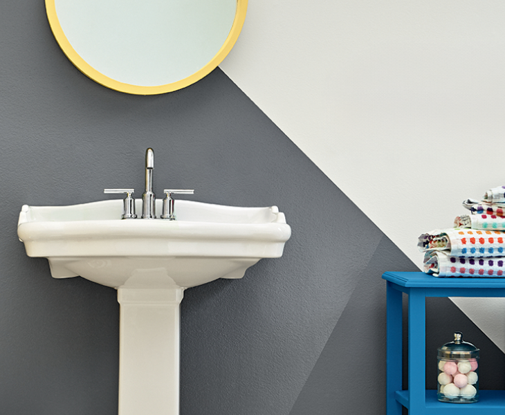 Bathroom vanity with a gold-framed mirror and shelving. Wall painted off-white and deep grey. 