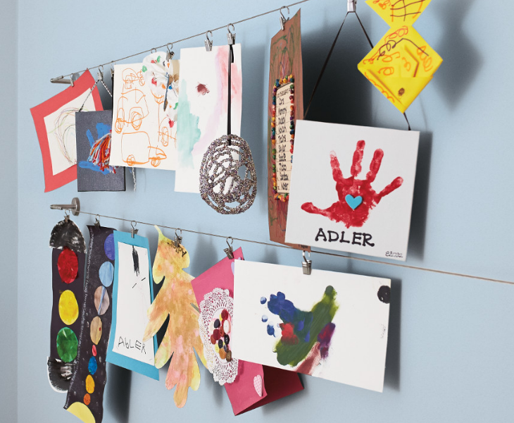 Café clips hold children’s artwork with café clips against a light blue wall.