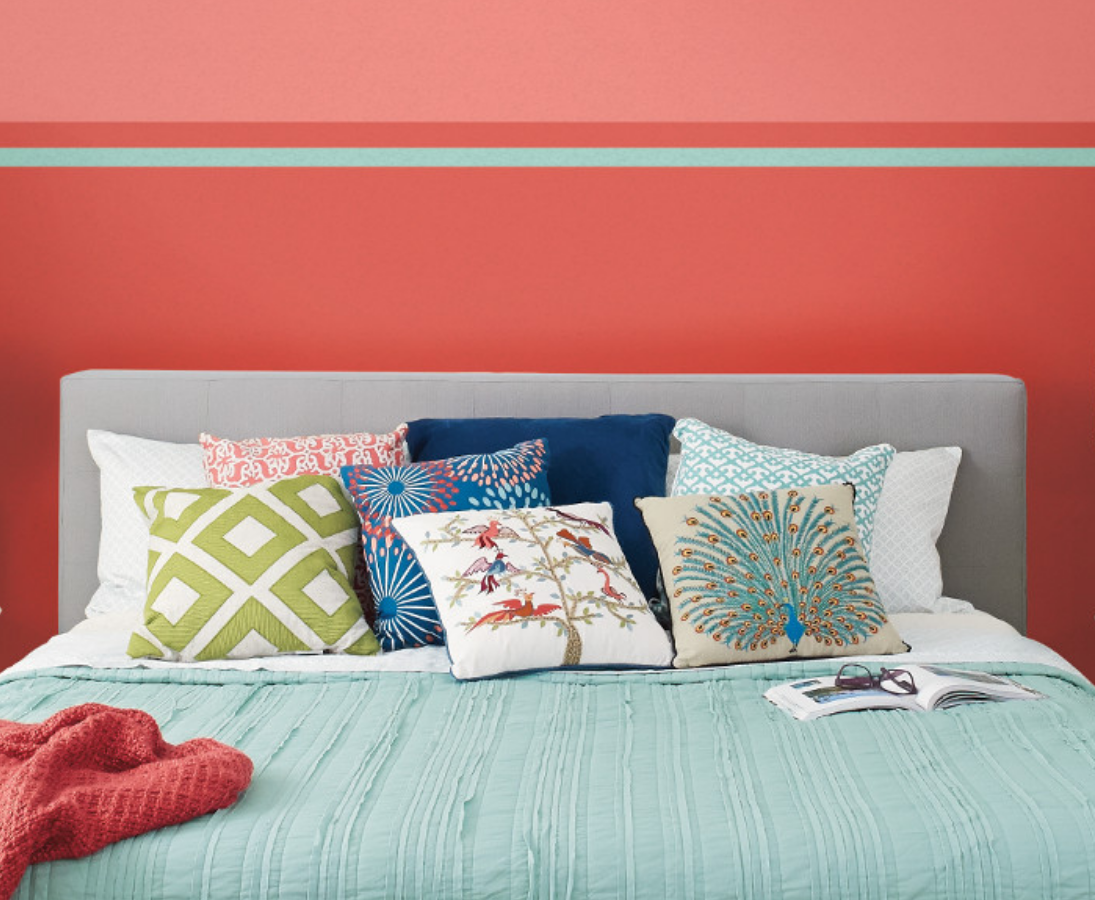 A sunny bedroom with subtle blue and green blankets and pillows. Walls painted carmela coral.
