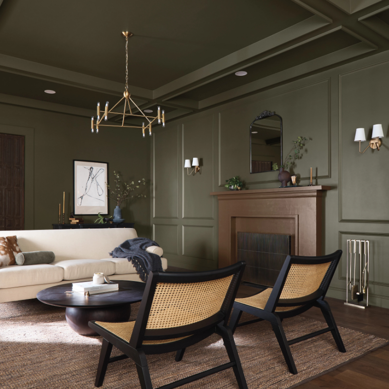 Beautiful traditional living room with dark green walls, modern furniture and a wooden mantel around a fireplace.