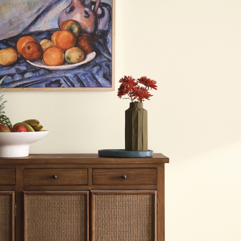 Ultra White painted living room, green vase of red flowers sits atop of a wood console table. Framed painting on the wall.