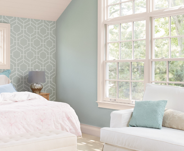 Sunny bedroom with geometric pattern on one wall, large windows and a love seat.