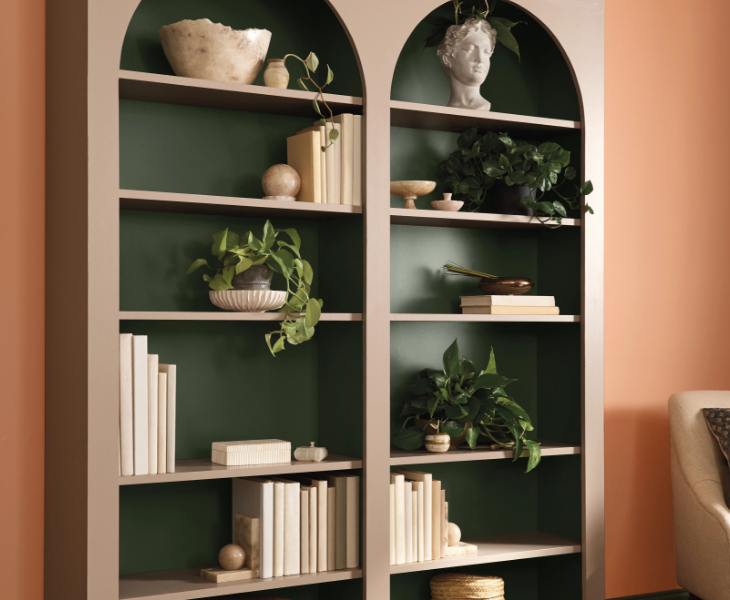 Curated shelving with arches at top. Back wall of shelving is dark green, shelves and frame are mauve, wall is wild orange.