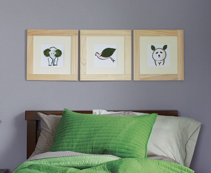 Child’s room, bed with green linens and grey walls with animal art prints in wood frames.