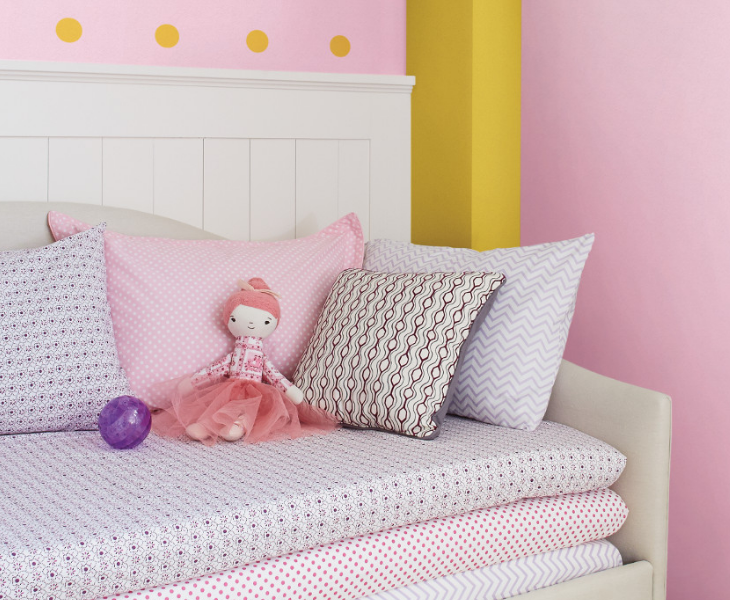 A toy doll sits on a trundle with patterned pillows and a playful yellow polka dot pattern on the wall.