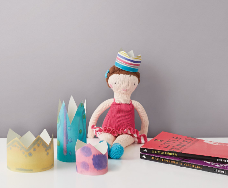 A toy doll with hat and dress sits on a white desk against a wall.
