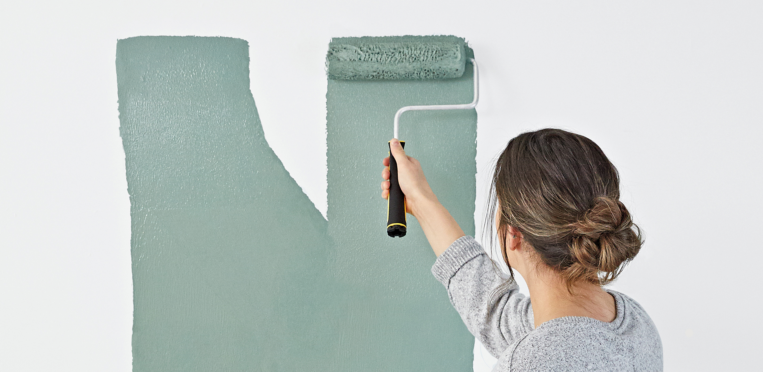 A person rolling teal colored Dutch Boy paint onto a white wall in an N shape.