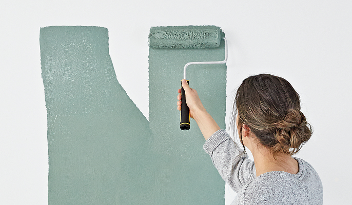 Woman rolling on green paint to a wall