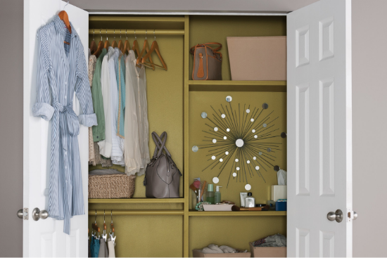 Open French doors reveal a woman’s wardrobe with shirts, purse, wall art, cosmetics and storage baskets.