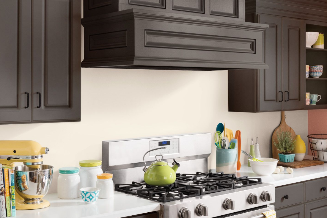A kitchen stove top and range with a green tea kettle. Backsplash is painted in a light-colored semi-gloss paint.