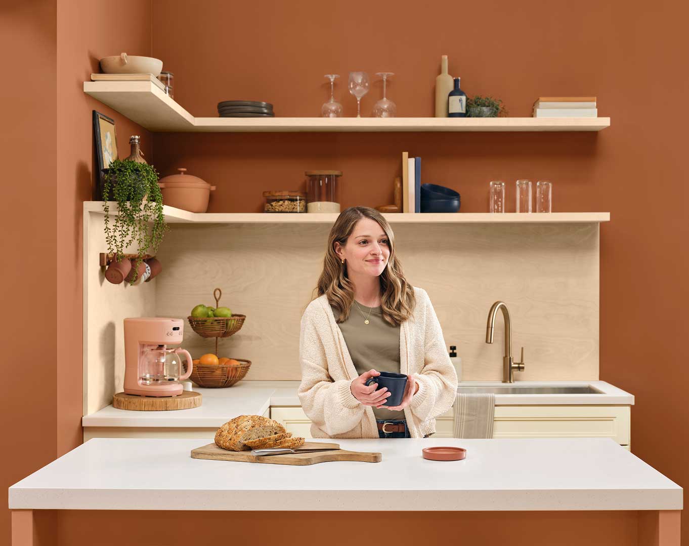 Person standing at a kitchen counter with a coffee mug and freshly baked bread.