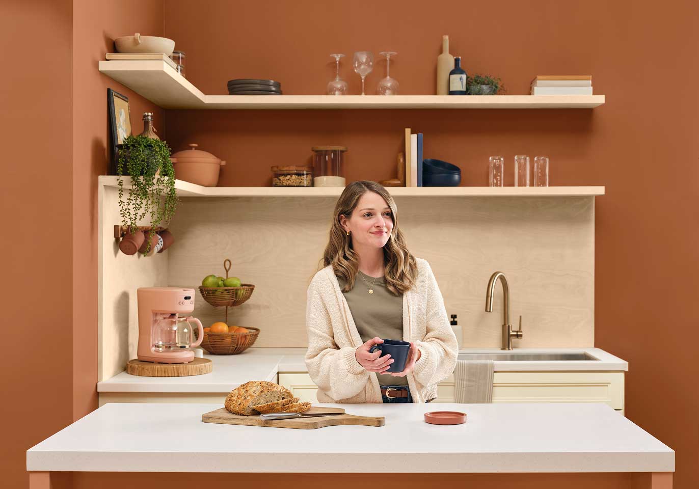 Person standing at a kitchen counter with a coffee mug and freshly baked bread.