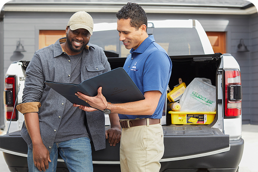 Two people standing in front of the bed of a pickup truck having a discussion.