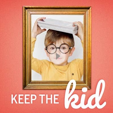 A picture of a small boy in glasses holds notebooks in a picture frame hanging on a pink wall. 