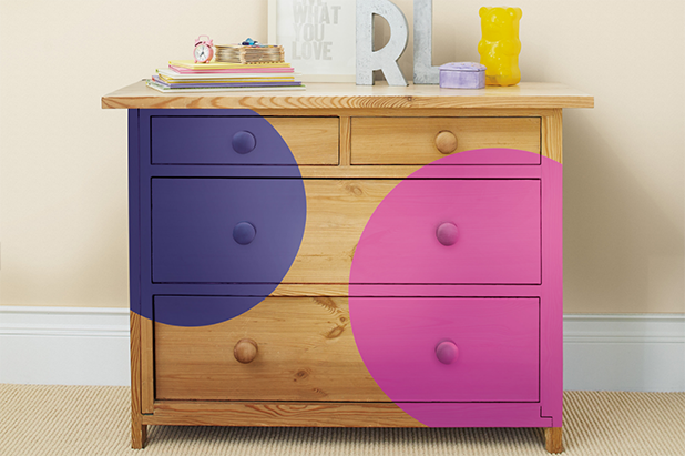 A warm wood bedroom dresser is painted with two large dots of color – one is purple and one is pink.