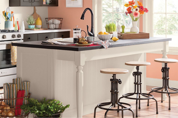 Brightly lit kitchen with island that has white cabinets and dark countertop. Walls painted native copper.