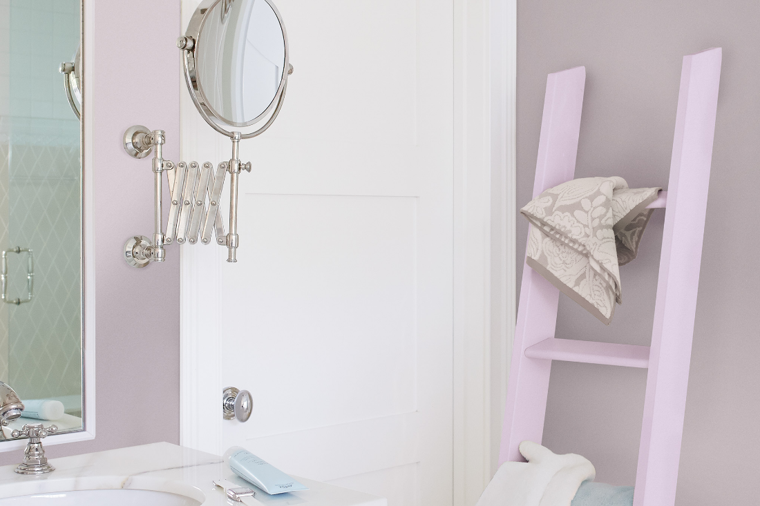 A light pink ladder shelf sits against the wall of a bathroom with traditional silver faucet and accessories on the vanity.