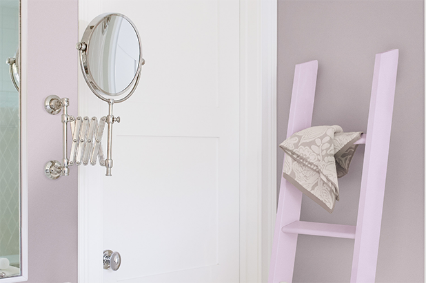 Light, lilac-colored shelf sits against the wall of a bathroom with traditional silver faucet and accessories on the vanity.