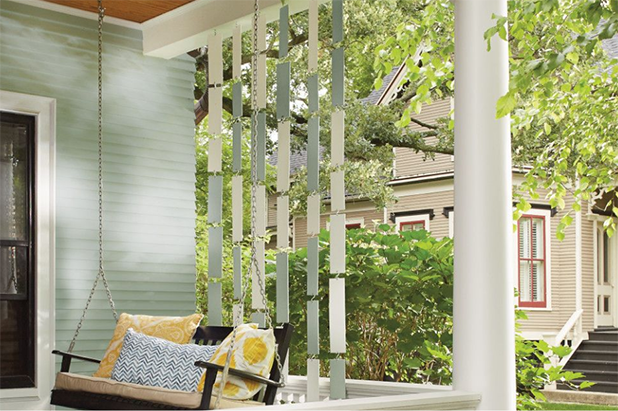 Front porch with swing bench and a divider wall of plywood panels painted multiple shades of green. Neighboring house adjacent.