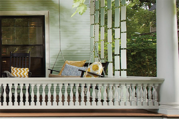 Front porch with swing bench and a divider wall of plywood panels painted multiple shades of green.