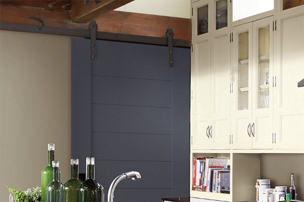 A barn door painted in the color flint stone, slides into a modern kitchen with light cabinets.