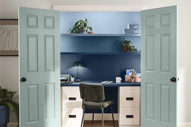 A home office situated inside of a closet with French doors painted light teal. Wall and shelves in office are darker blue. 