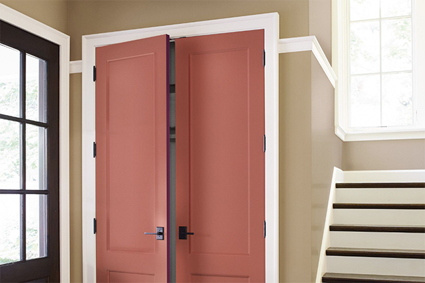 Red closet doors slightly ajar, near a front door, stairs lead upward. Walls painted aged clay.