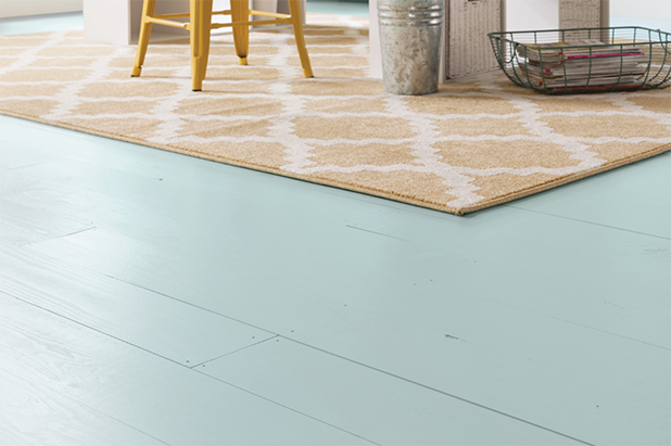 A floor painted in the color minted ice with a yellow patterned area rug and yellow chair.